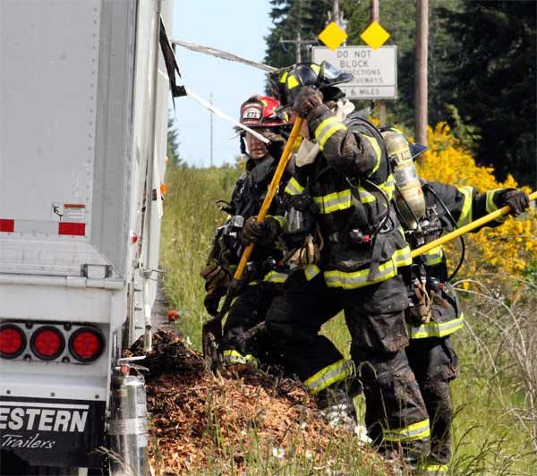 Emergency responders from the Poulsbo Fire Department work to extinguish any remaining flames or smoldering wood chips May 25 after a trailer caught fire on Highway 3