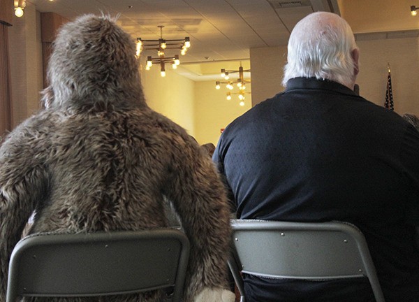 A man sits beside a stuffed Bigfoot at the first ever Bigfoot Habituation Research Conference at the Baymont Inn & Suites.
