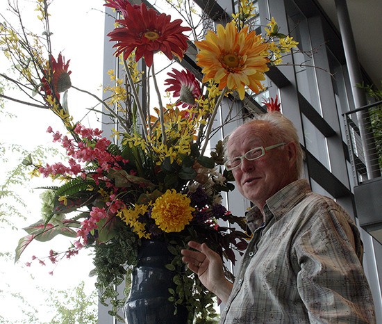 Bremerton resident Gordon Andrews stands in front of his most recent floral arrangement at the Norm Dicks Government Center. The retired florist provides arrangements at no cost.