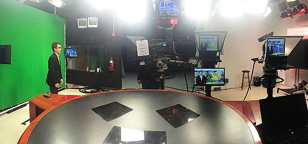 Weatherman Matt Leach stands near a green screen and television cameras while on a set.