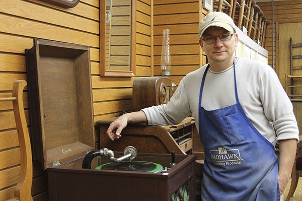 Paul Derevnin stands in his Bremerton shop next to an old crank phonograph which he recently acquired. He’s planning on refinishing it
