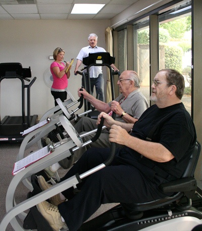 Exercise Specialist Kellie Greenhill (back) checks Gary Hoffmann's vitals while other clients continue their workouts at CAPRI Heart & Lung Institute in Bremerton.