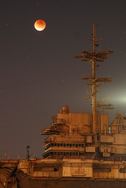 The moon rises over the USS Independence (CVA-62) in Bremerton during a lunar eclipse Sept. 27. The moon took on a red-orange hue during the eclipse. The reddish hue is due to the way that sunlight is refracted as it passes through Earth’s atmosphere while the moon is in Earth’s shadow.