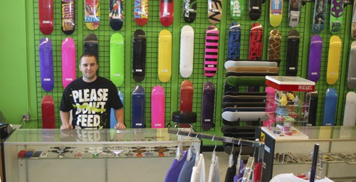 Richard Anderson stands in front of a wall of skateboards at the new Mile Hill location of his business