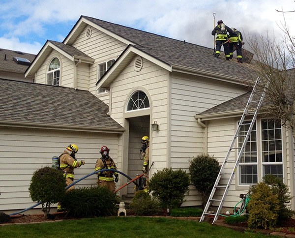 Firefighters work at the scene of a structure fire at 11000 Peony Place NW in Silverdale on March 24. They cut a hole into the roof to clear smoke from the building.