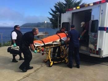 A Coast Guard Station Neah Bay crew member assists local emergency medical services with the transfer of a Port Orchard diver rescued off Cape Flattery.