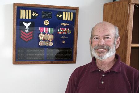 Kitsap resident and retired nuclear submarine commander Capt. Tom Rogers stands next to a military awards shadow box displayed in his Poulsbo home.