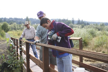 Volunteers Tex Lewis and Doug Ludwig help Olympic College Running Start student Daniel Hnatovic install hand railings Wednesday on a new Clear Creek Trail bridge.