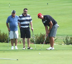 A golfer putts as fellow teammates look on.