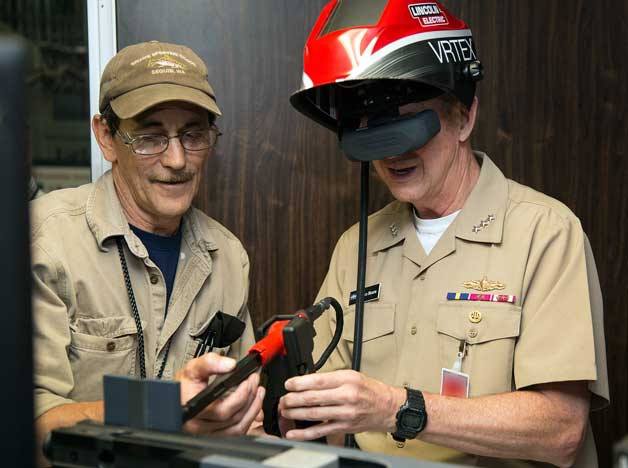 Puget Sound Naval Shipyard and Intermediate Maintenance Facility Shop 26 Work Leader Scott Penson (left) demonstrates a virtual welding simulator to Vice Adm. Thomas Moore
