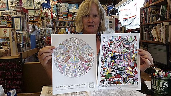Suzanne Droppert at Liberty Bay Books displaying a couple of the coloring pages available in Johanna Basford’s books.