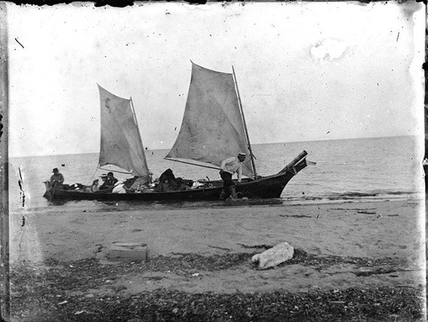 A canoe with sails pulls ashore in this old
