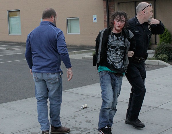 The bloody suspect in an alleged stabbing attempt near SEEfilm Cinema is led away by Bremerton Police officer Tim Garrity. Jay Kent