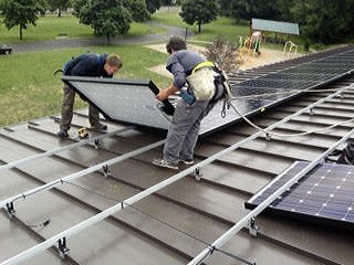 Workers install solar panels on the roof of Village Green Community Center earlier this month.