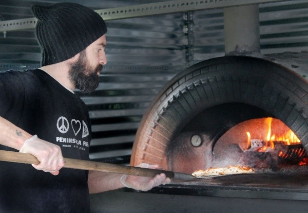 Peninsula Pies co-owner Scott Williams removes a pie from the portable wood-fired oven