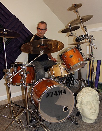 Lance DeMers gets behind his drum set in his house.  The musician now teaches private drum lessons.