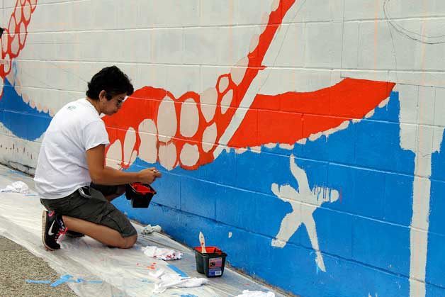 A woman helps paint the mural on the back of the Peninsula Community Health Services building June 25.