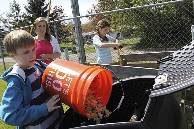 Brownsville Elementary student Devon William pours compost into a tumbling compost bin as teacher Rochelle Lancaster and student Olivia McFall watch. The trio participates in Green Club