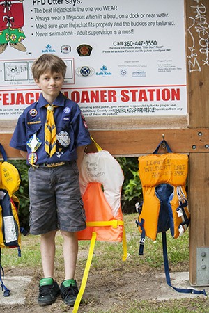 Ryan Stevens stands in front of a life jacket loaner station at Island Lake last Saturday. Ryan is looking for donations to help fund the stations at lakes and beaches around the county.