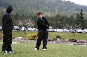 Bremerton senior Aimee Connolly looks on as fellow senior Hannah Crawford works on her swing Tuesday at Gold Mountain Golf Complex .