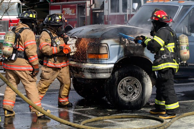 Poulsbo firefighters use a power saw and pry bar to open the hood of a burning Ford F250 in the Poulsbo Central Market parking lot Friday.