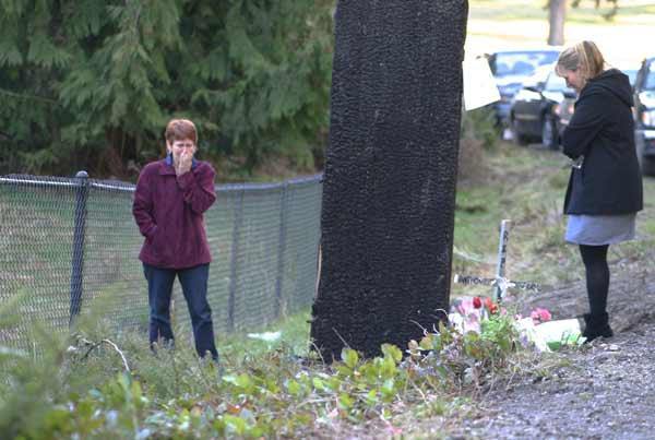 Visitors to the site of the accident pay their respects on Tuesday on NW Finn Hill Road. A memorial at the base of the utility pole continues to grow.