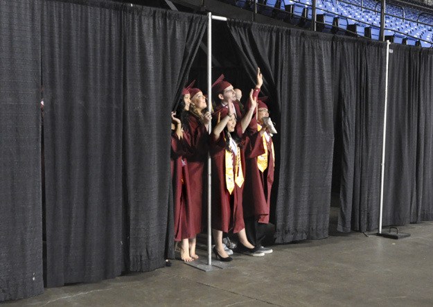 Soon-to-be graduates peer from behind a curtain to see and wave at family and friends gathered in the stands at the Tacoma Dome for South Kitsap High School's graduation ceremony.