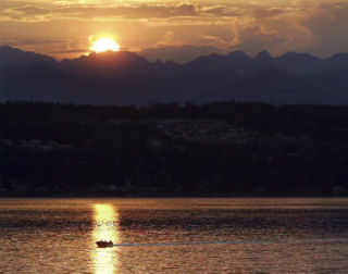 A boat jets across Dyes Inlet as the sun sets behind the Olympic Mountains.