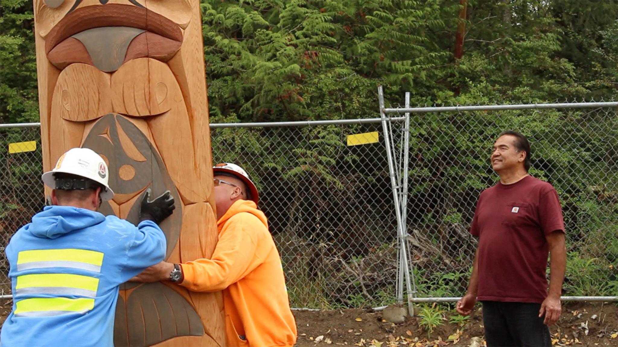 Skokomish artist Andy Wilbur-Peterson watches as crews install his totem pole, “Blue Jay & Bear,” Quinn Brein / Courtesy