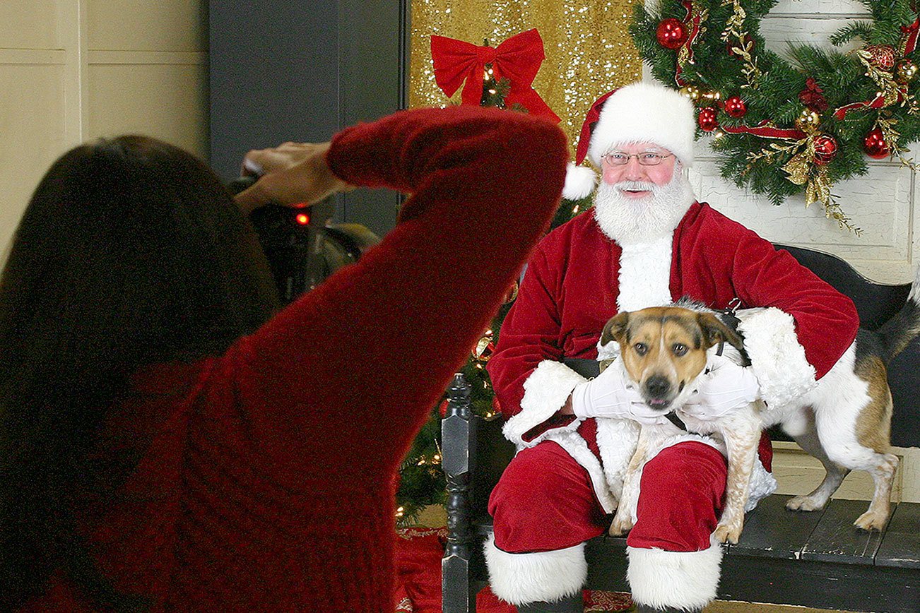 Mary Eklund, left, of Four Foot Photography photographs Santa Jeff Berger with a dog at Kitsap Humane Society’s Santa Paws event Dec. 11.                                Michelle Beahm / Kitsap News Group