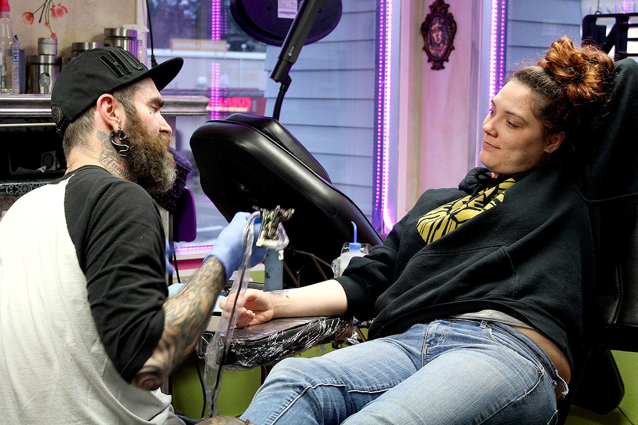 Paul Weaver tattoos Chelsey Freeman with flash art. Michelle Beahm / Kitsap News Group