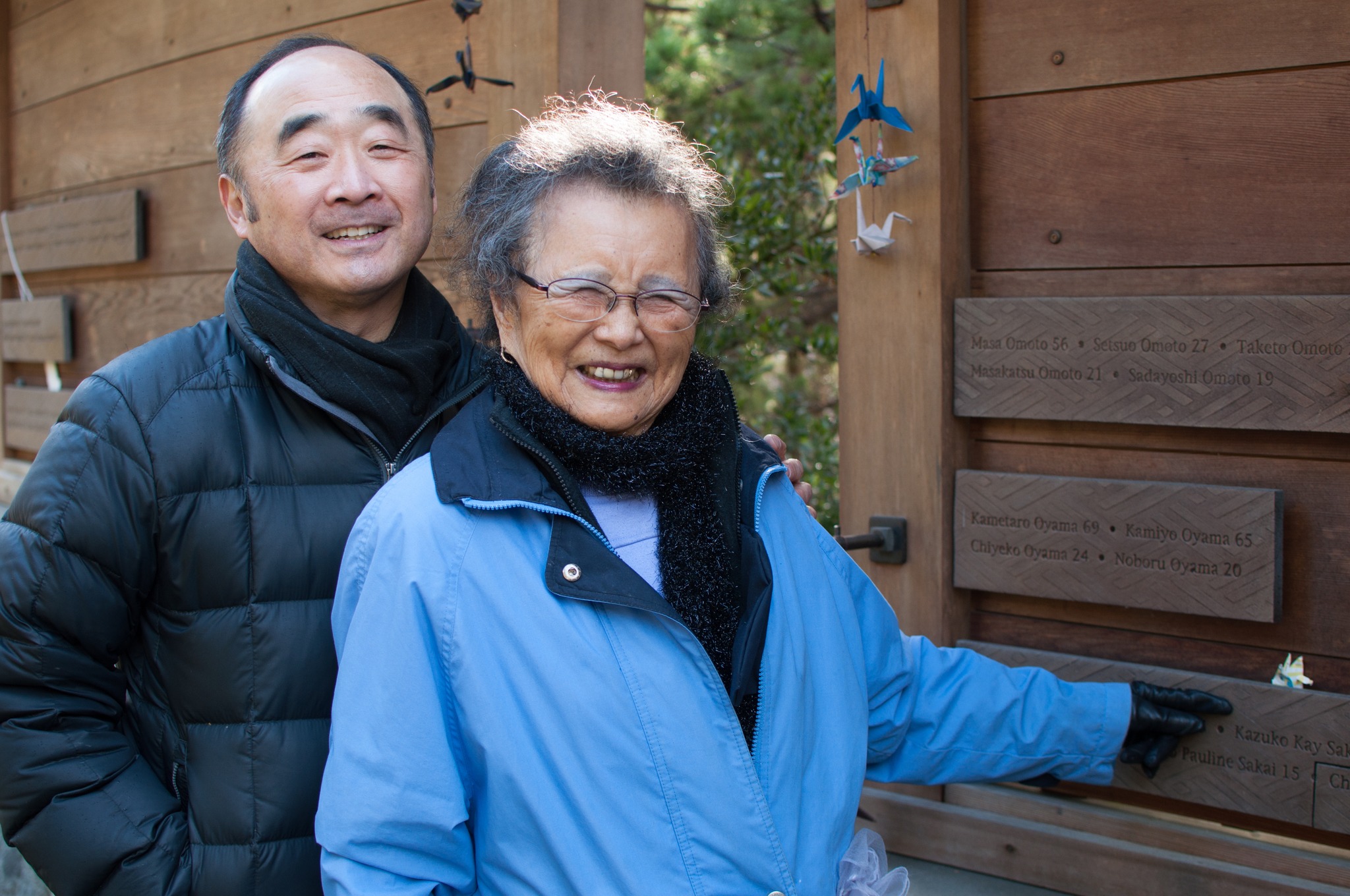 Kay Sakai points at her name on the Bainbridge Island Japanese American Exclusion Memorial, which includes the name of every Japanese American resident of the island removed under Civilian Exclusion Order No. 1. Behind her stands Clarence Moriwaki, founder of the Bainbridge Island Japanese American Exclusion Memorial. (Enrique Pérez de la Rosa/WNPA Olympia News Bureau)