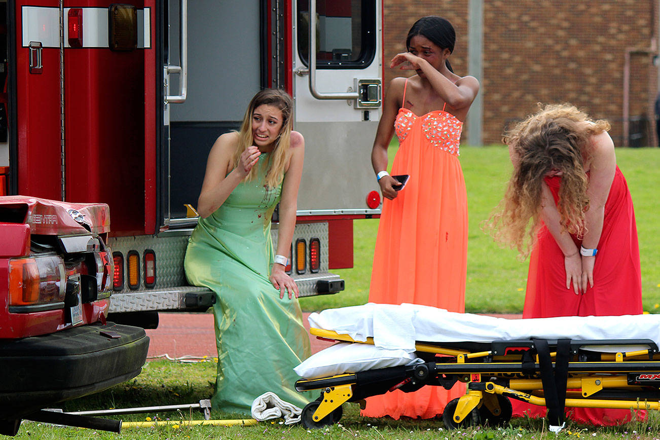 Emma Gutierrez, left, Kennedy Jackson, middle, and Kasey Morris, right, watch as their fellow students are triaged and tended to by Central Kitsap Fire and Rescue in a mock crash held April 25 at Central Kitsap High School. The crash is designed to raise awareness of and deter people from driving while under the influence or driving distracted.                                Michelle Beahm / Kitsap News Group