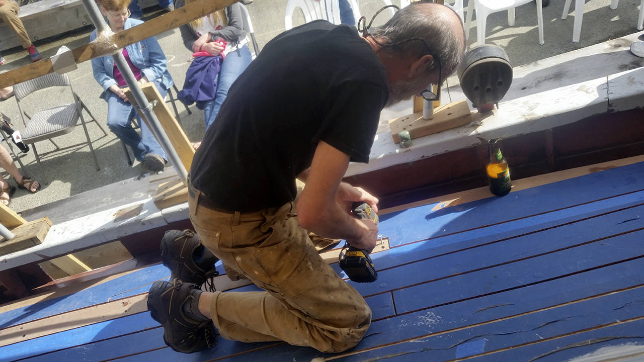 Shipwright Scott Kimmett puts in the final screws fastening down the last plank — the “whiskey plank” — on the deck of the Kitsap tall ship, “Fiddler’s Dream,” that is undergoing reconstruction at the Brownsville Marina. The blue masking tape on the deck planks is to keep them clean when workers caulk the seams between the planks with cotton yarn and caulking compound. The caulking between the boards will allow the deck to remain waterproof even when the wood planks expand or shrink.                                Terryl Asla|Kitsap News Group