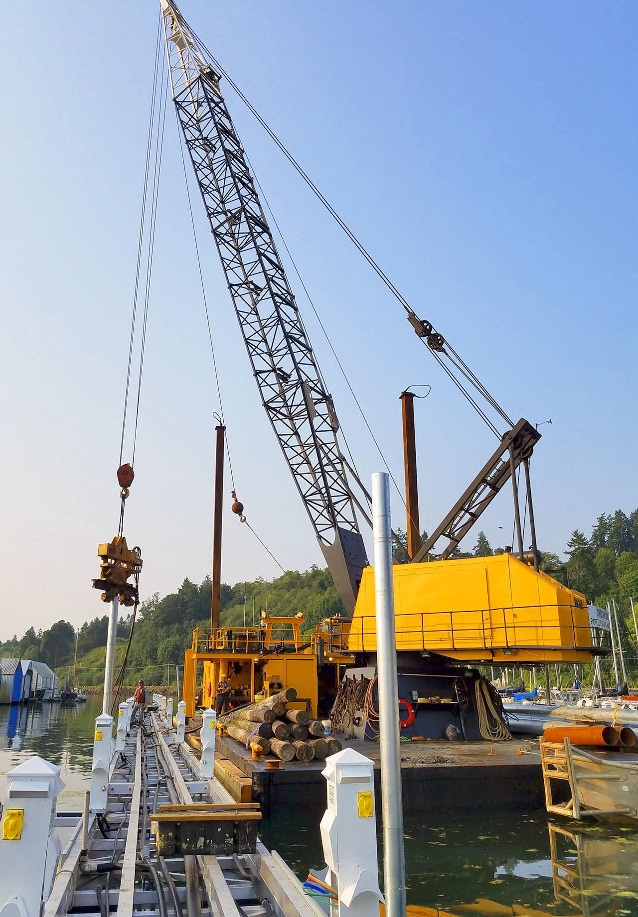The pile-driving crane places a new galvanized steel piling. The old, creosoted wood pilings the Skookum’s crew pulled earlier are stacked on the barge’s deck.                                Terryl Asla/Kitsap News Group