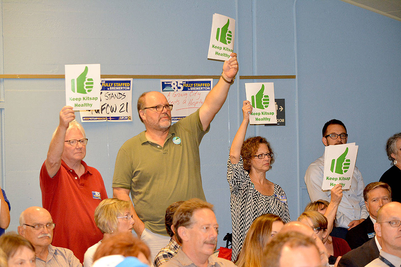 Members of the audience display signs that oppose the closure of Harrison Bremerton hospital. (Mark Krulish/Kitsap News Group)