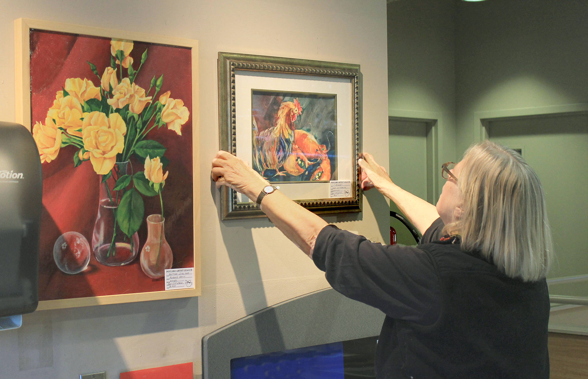 Lone Hansen straightens PAL fellow members hangings at Central Markets upstairs cafe.