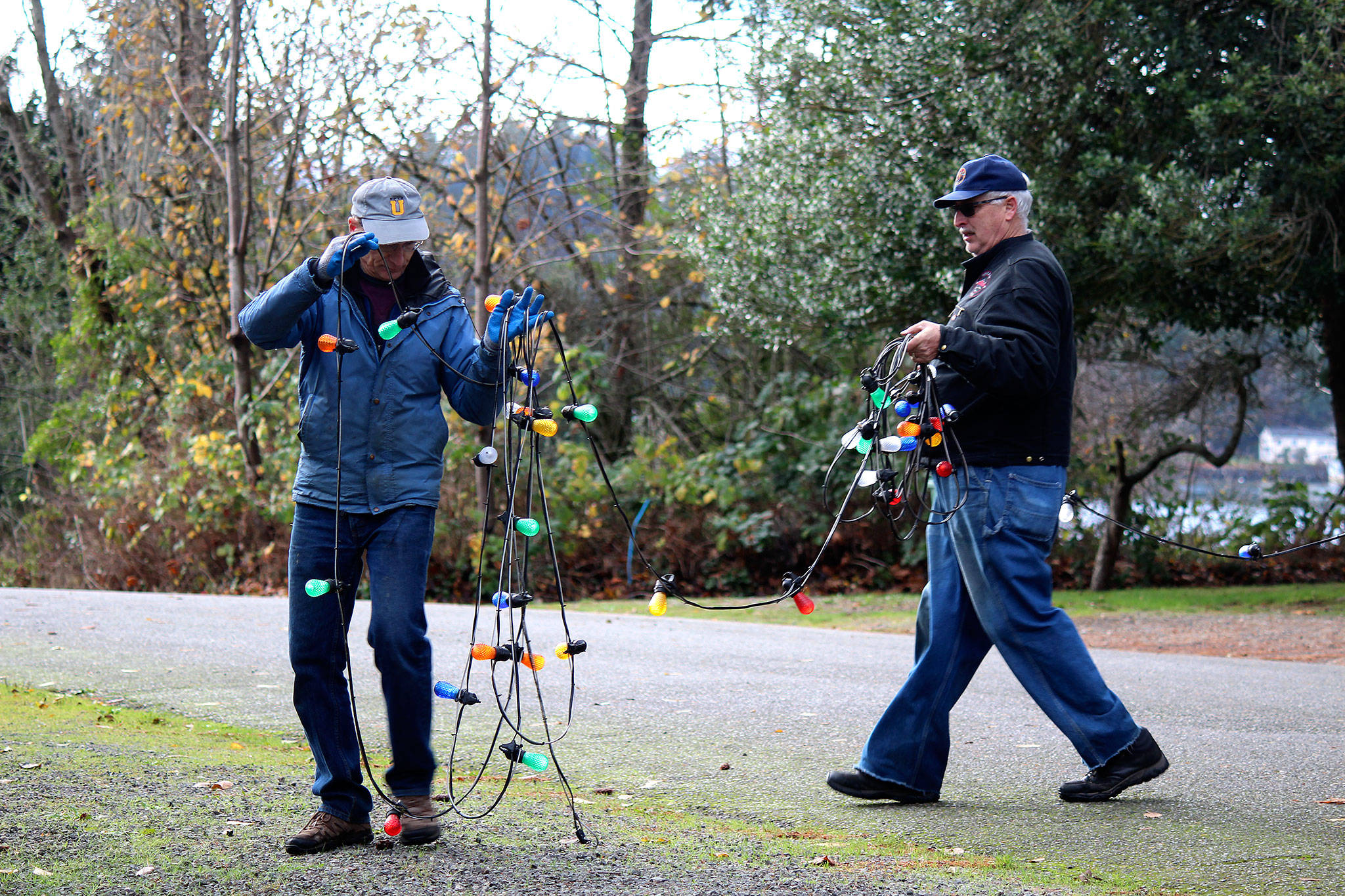 Kurt Tufford, left, and Bob Carter carry string lights across the street to ensure the community tree is lit up on all sides.                                Michelle Beahm / Kitsap News Group