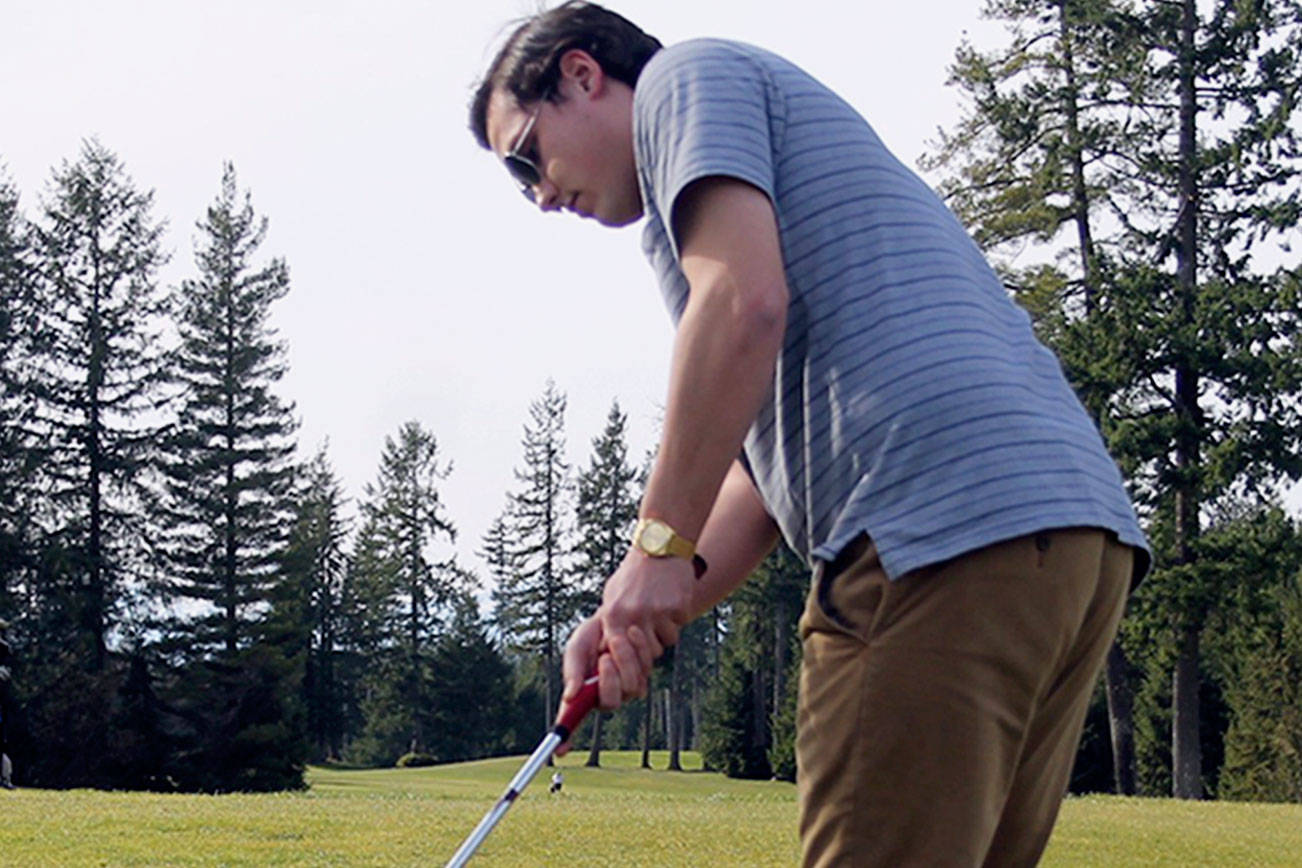 Senior Connor Lowe putting during a March 12 practice at Gold Mountain Golf Course while teammate Joel Angkico watches.