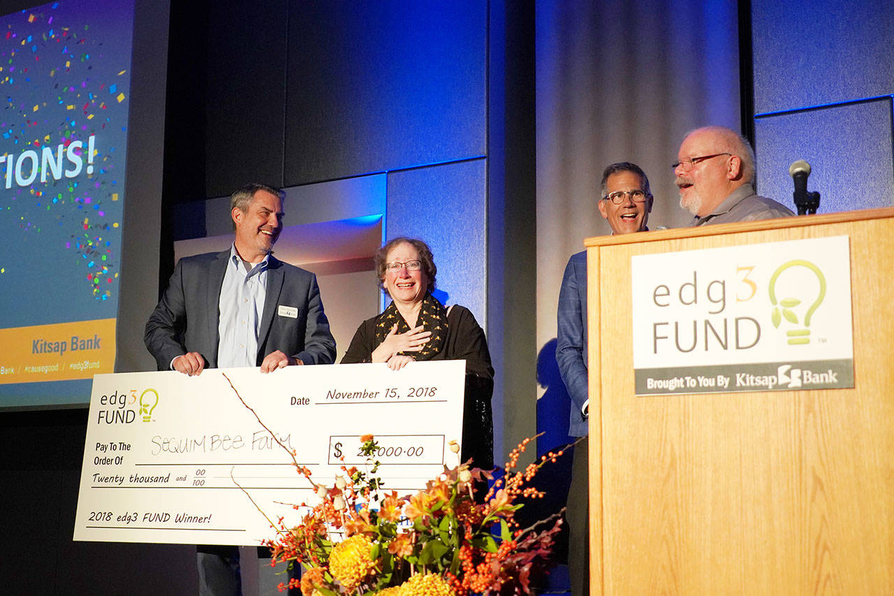 Meg Depew (center) of Sequim Bee Farm of Port Angeles accepts the grand prize of $20,000 in the annual edg3 FUND small business competition at a ceremony in Bremerton. Co-owner Buddy Depew is at the podium. At each end is Tony George (left), Kitsap Bank president and COO, and Steve Politakis, Kitsap Bank CEO. The competition was sponsored by Kitsap Bank. (Kitsap Bank photo)