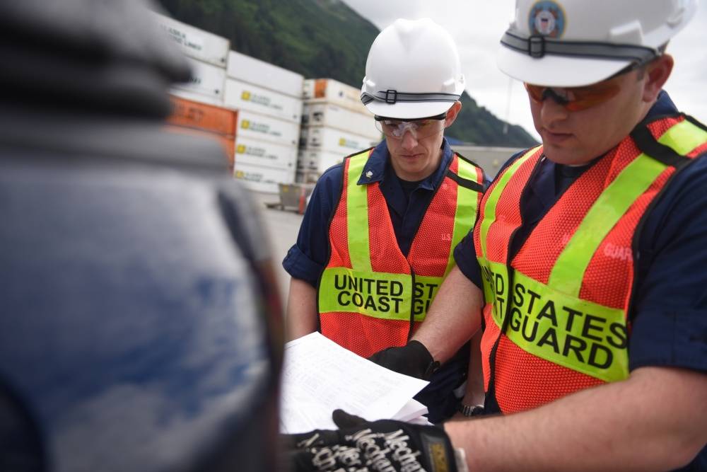 Petty Officer 3rd Class Lewis Beck and Petty Officer 2nd Class Chris Houvener, both marine science technicians at Coast Guard Sector Juneau, look through federal regulations during a container inspection in Juneau, Alaska, June 19, 2015. Coast Guard inspectors follow rigid, standardized regulations to ensure maritime operators across the country are held to the same rules. U.S. Coast Guard photo by Petty Officer 2nd Class Grant DeVuyst.