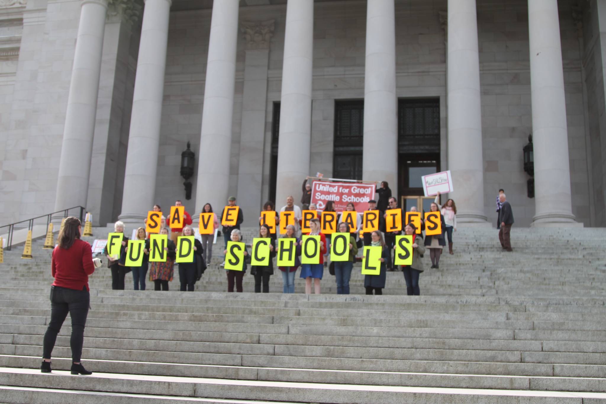 Seattle Public School’s librarians hold up signs on the capitol building steps, in protest of funding cuts that have resulted in cuts to libraries. Kate Eads, who organized the event, can be seen holding a megaphone addressing the group.—Photo by Emma Epperly, WNPA Olympia News Bureau
