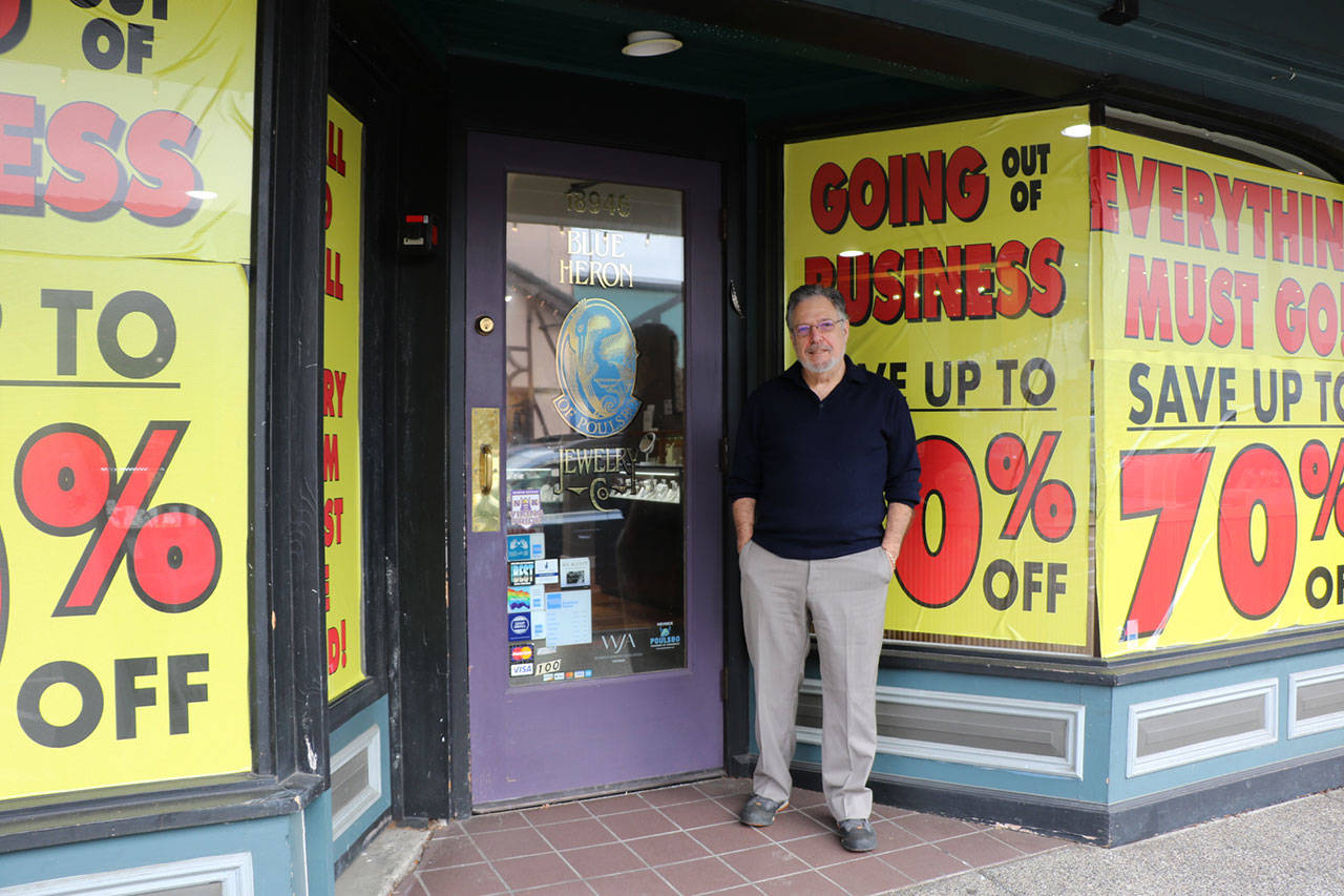<em>Leo Fried stands among the bright yellow signs that announce the retirement sale at his shop, Blue Heron Jewelry.</em>                                Ken Park/Kitsap News Group