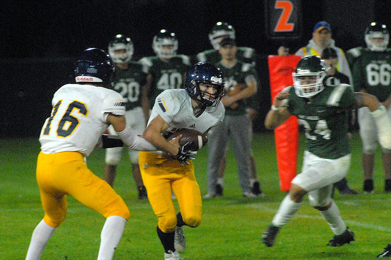 Bainbridge quarterback Jack Grant, left, hands off to Garrett Goade as Port Angeles defender Jeremiah Hall closes in on Friday night in Port Angeles. (Keith Thorpe/Olympic Peninsula News Group)