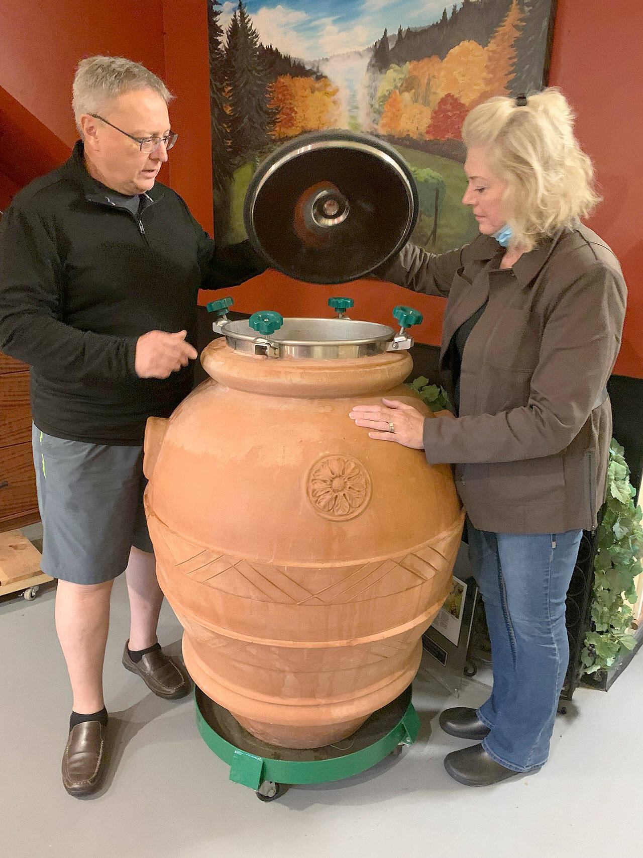 Stuart Chisholm and Mary Ellen Houston peer inside a large clay pot, where the juice of the grapes will ferment. (Bob Smith | Kitsap Daily News)