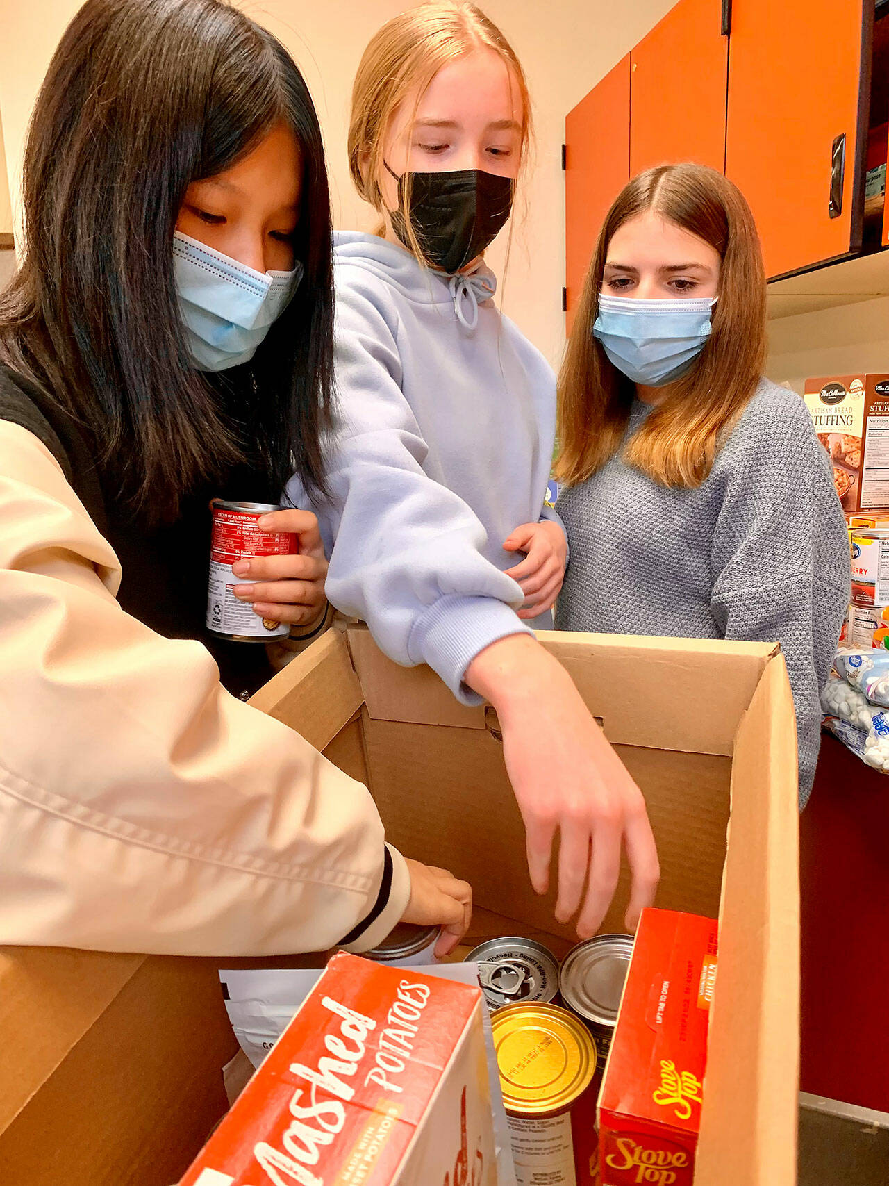 Kai Zhong (left), Ellie Wright and Aisha Sorter look over food items that were collected for Sedgwick Middle School’s “Holiday Help” Thanksgiving food drive. (Bob Smith | Kitsap Daily News)