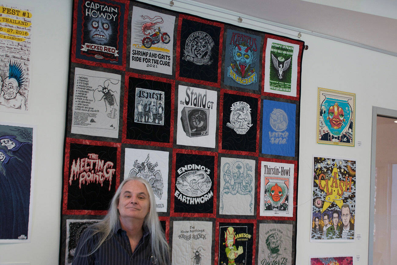 Tyler Shuey/North Kitsap Herald
Local freelance artist Pat Moriarity stands next to a quilt his aunt made that includes many of his creations over the years.
