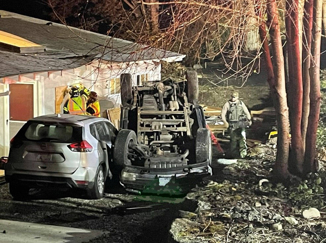 Firefighters work to board up a broken window while a sheriff’s deputy investigates the scene after a pickup came off of West Kingston Road, injuring its driver and causing significant damage to a home and an adjacent parked car Nov. 10. Courtesy Photo