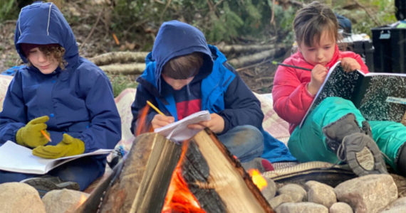 Students write in journals around a campfire at WildWise School. Courtesy Photos