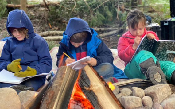 Students write in journals around a campfire at WildWise School. Courtesy Photos